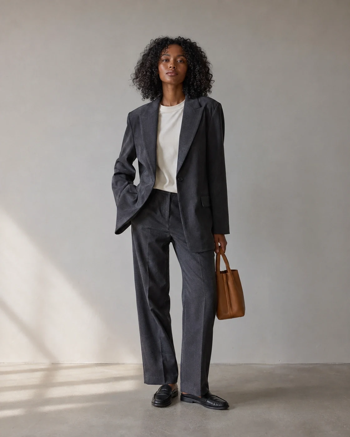 The same model and charcoal suit against a light-grey studio after changing the terracotta background